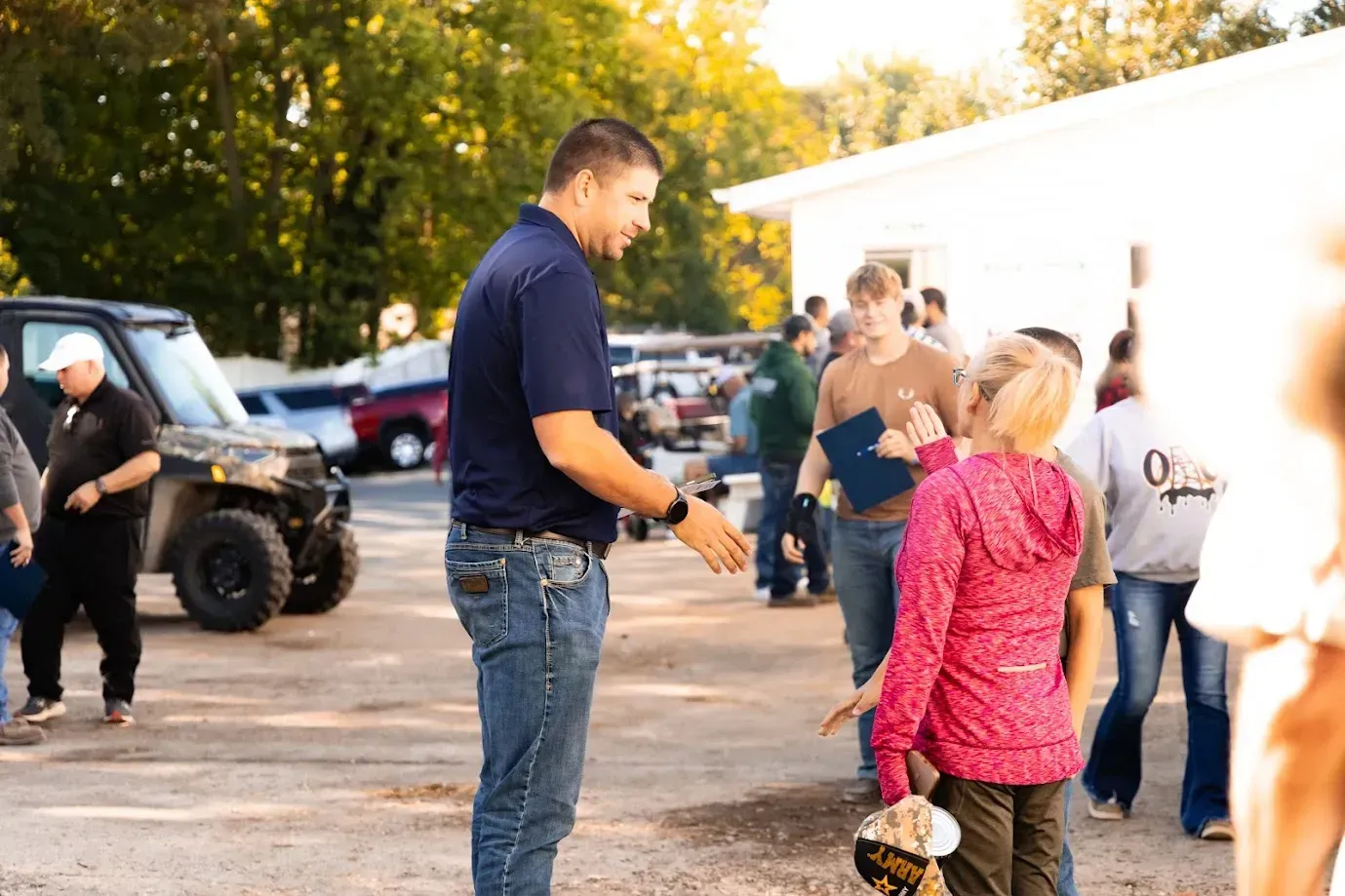 People standing and talking outdoors near parked vehicles in a sunny lot