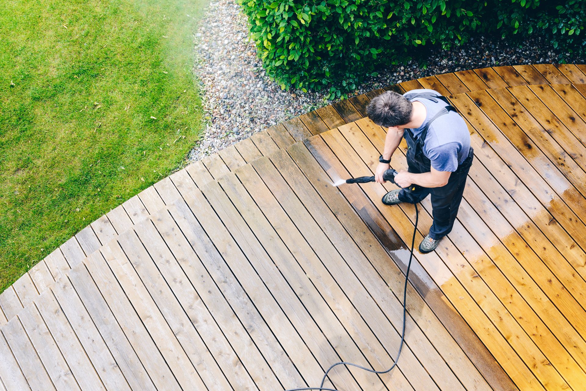 A man is cleaning a wooden deck with a high pressure washer.