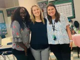 Three women are posing for a picture in a classroom.