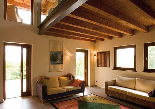 Soggiorno con soffitto con travi in ​​legno, due divani, ampie finestre e un tappeto orientale.