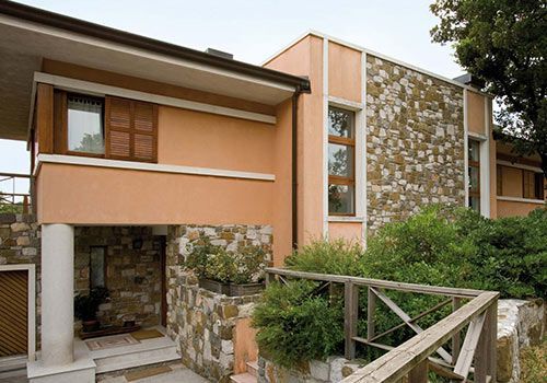 Casa a due piani con stucco color pesca chiaro e dettagli in pietra, persiane in legno e ringhiera in legno.