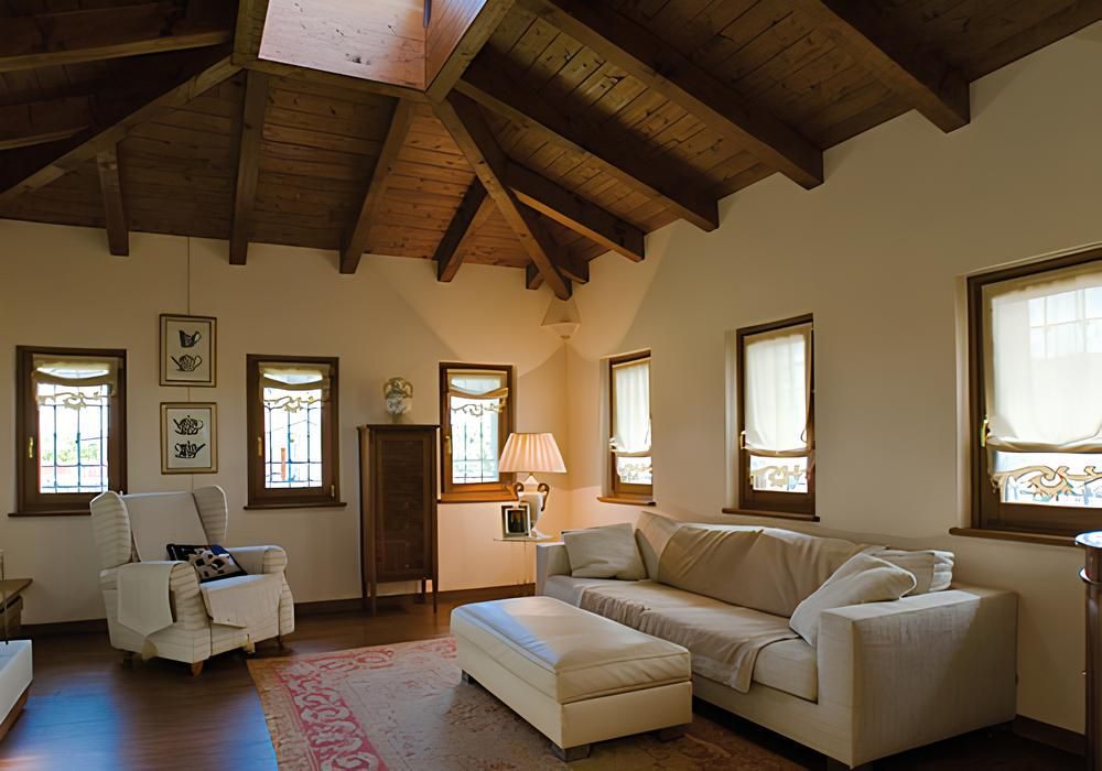 Soggiorno con soffitto in legno, finestre, mobili, tappeto e pareti di colore chiaro.