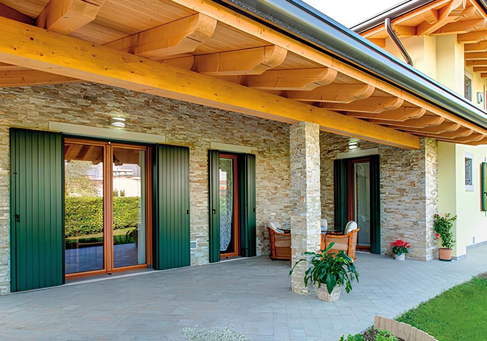 Patio con pareti in pietra, persiane verdi, travi in legno e vista sul cortile.
