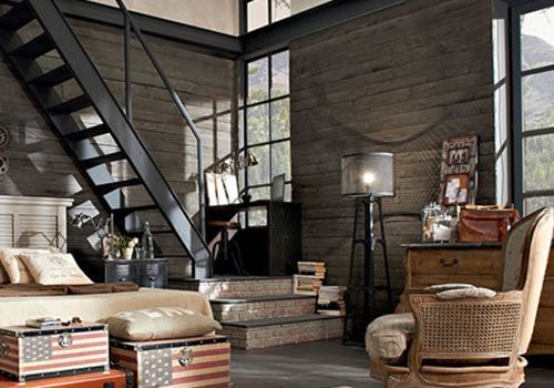 Camera da letto soppalcata con scala industriale, pareti in legno, bauli con bandiera americana e vista sulle montagne.