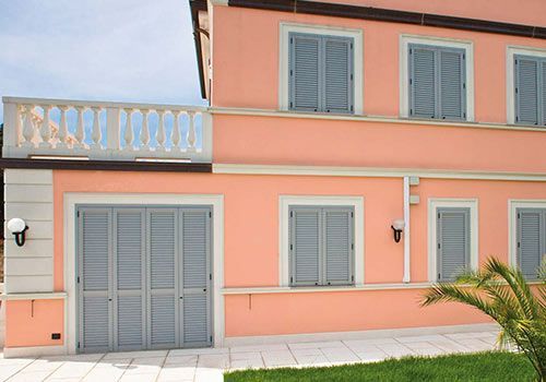 Edificio color pesca a due piani con persiane grigie e un balcone bianco.