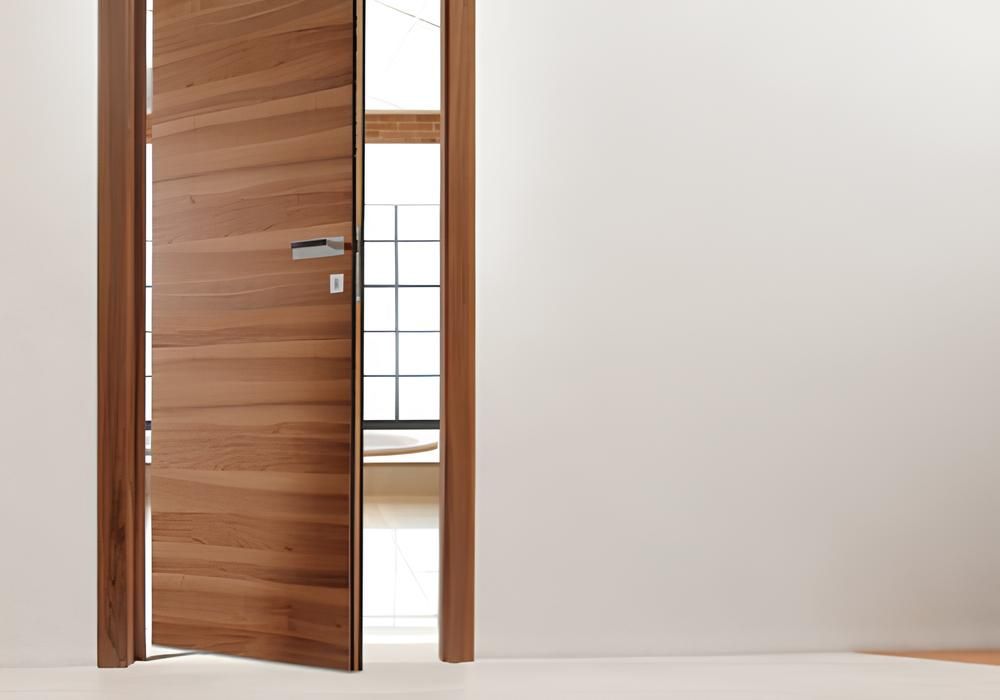 Porta di legno, parzialmente aperta contro il muro bianco, con luce intensa visibile attraverso l'apertura.