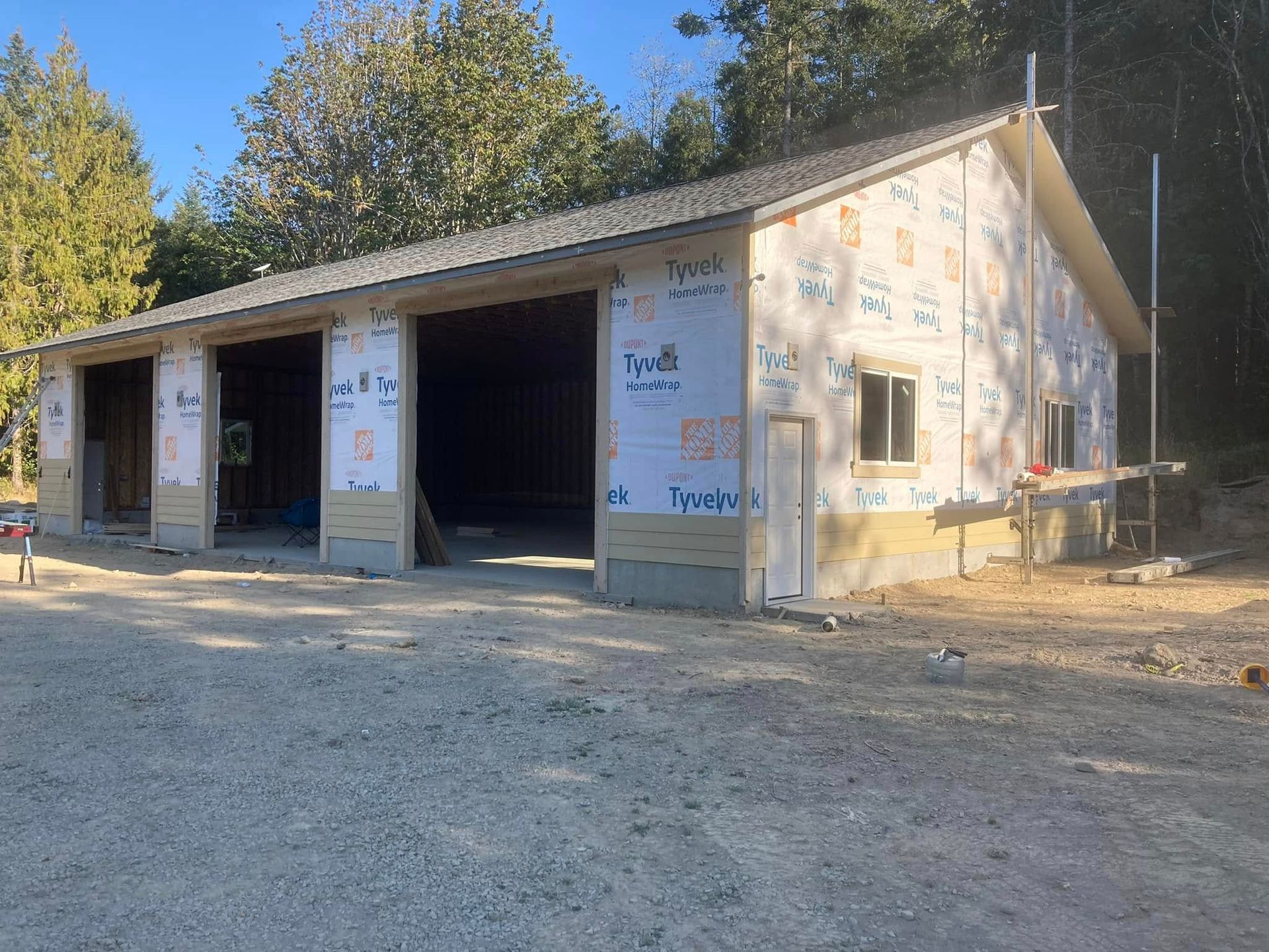Garage under construction with three bays, exterior walls covered in Tyvek, and gravel driveway.