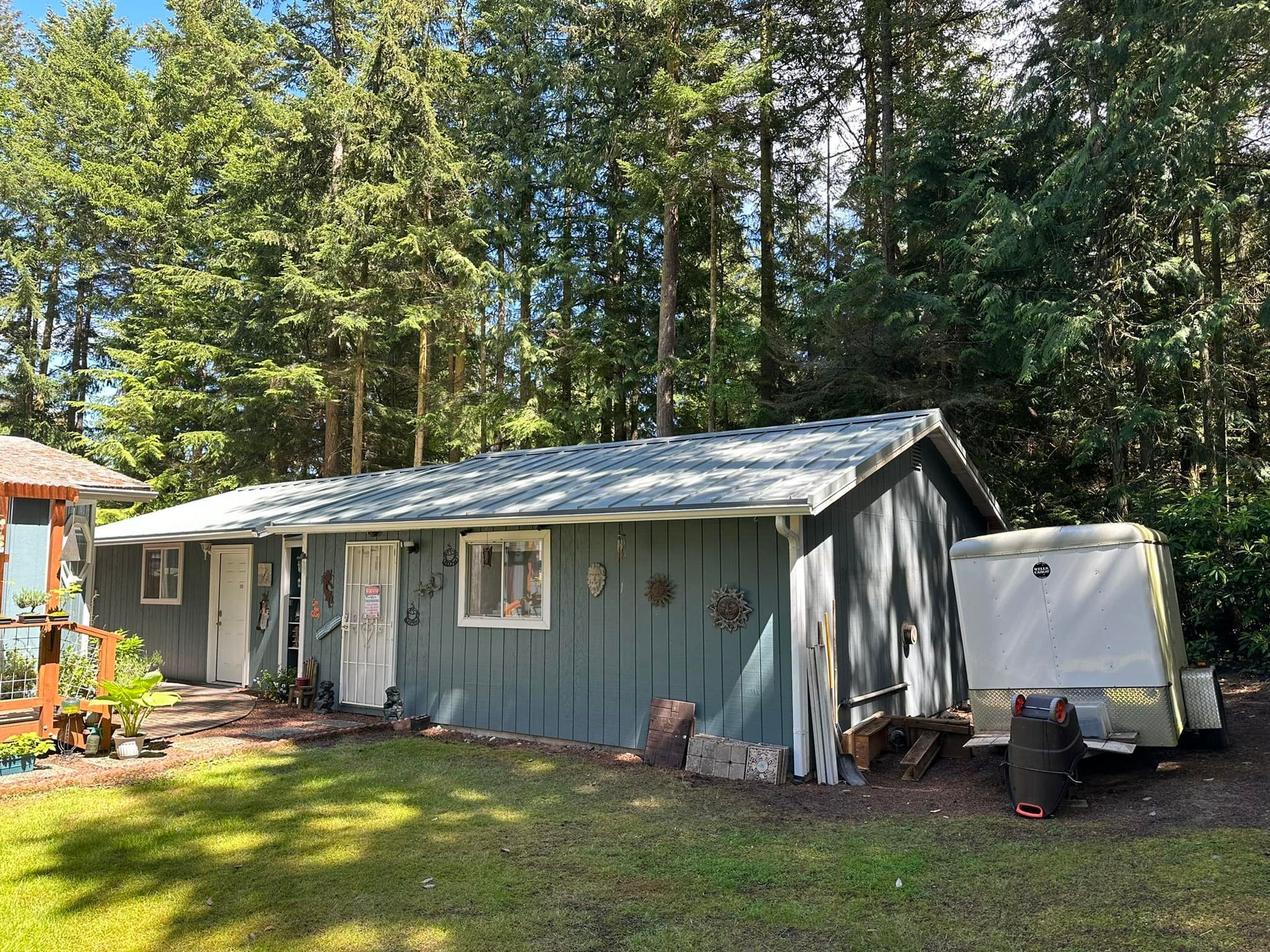 Blue-sided, one-story building with a light gray roof and trailer parked in front; trees in the background.