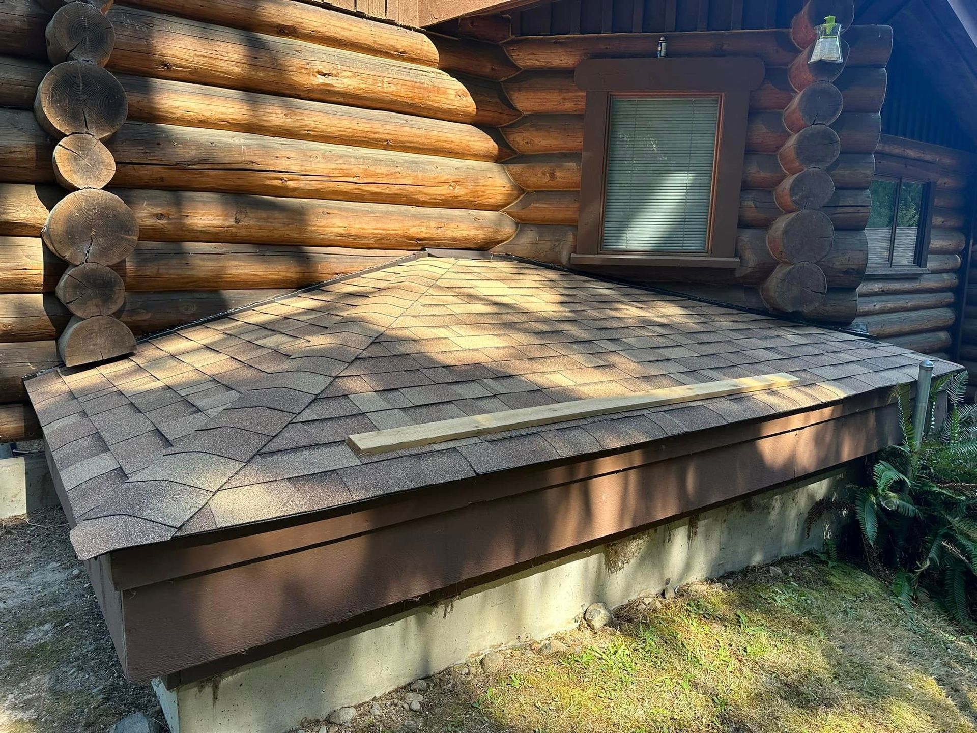 Brown shingled roof over a low, brown-sided structure attached to a log cabin.