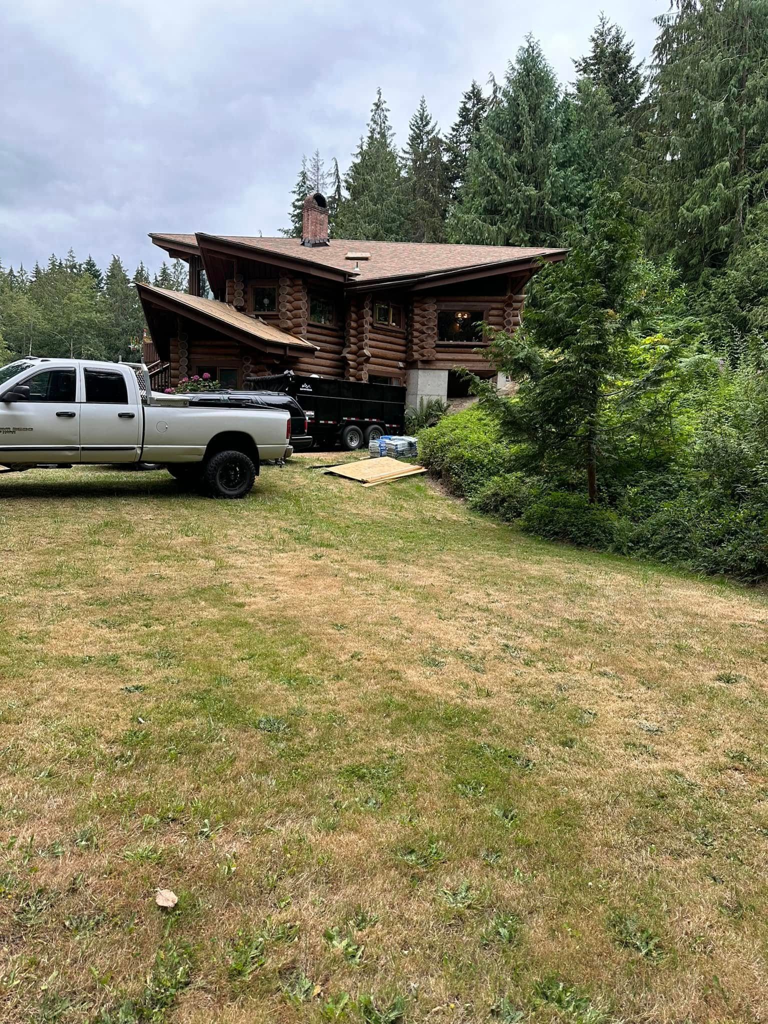Log cabin with pickup truck in the yard, surrounded by trees under a cloudy sky.