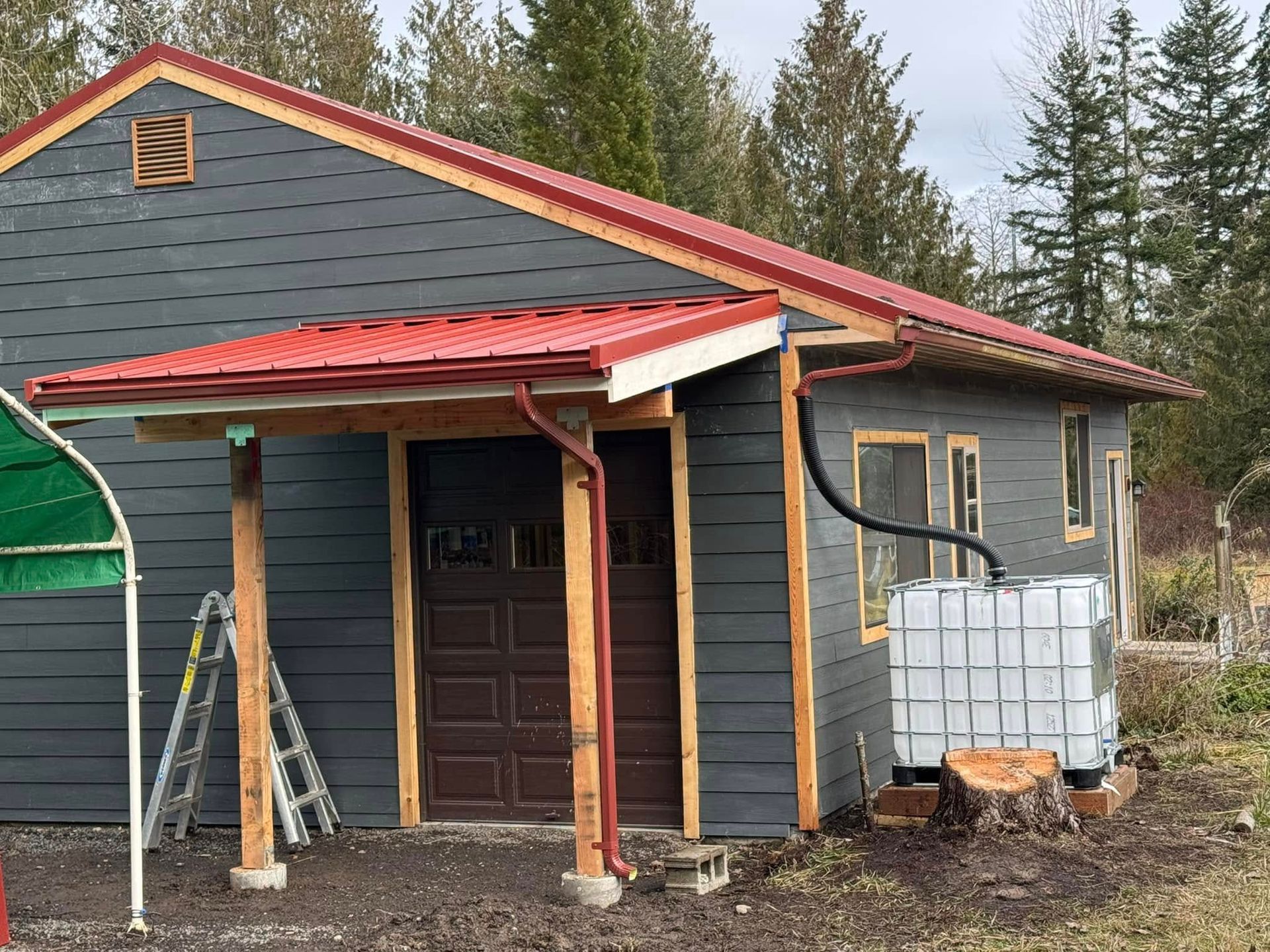 Gray building with red roof, wooden posts supporting a porch, and a water tank.