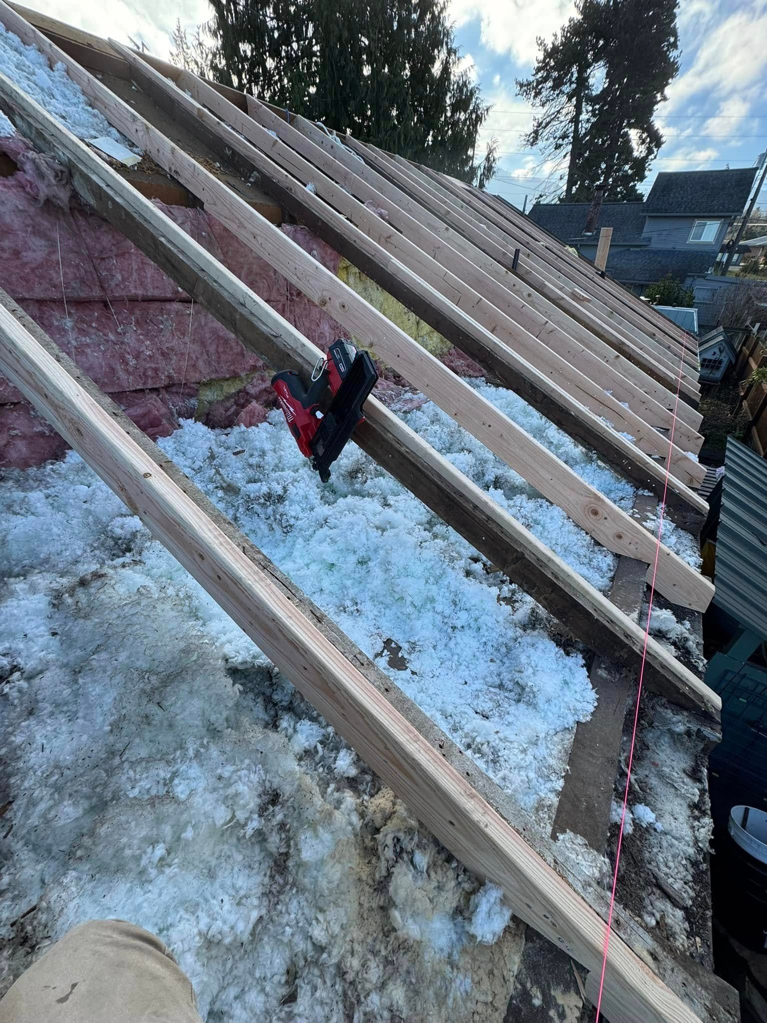 Roof rafters with insulation and a nail gun, exterior view.