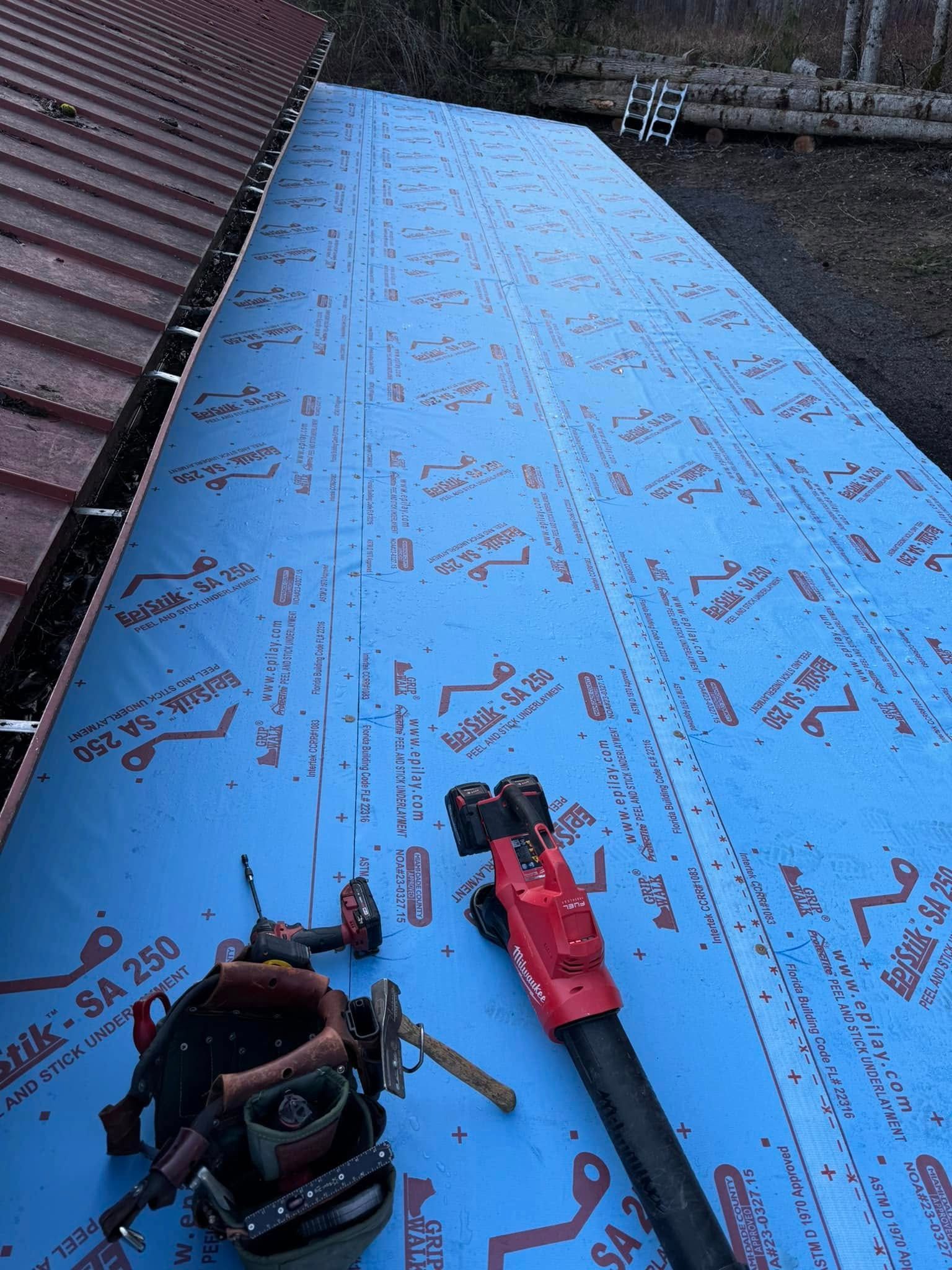 Roof underlayment being installed; blue material on a roof, tools visible.