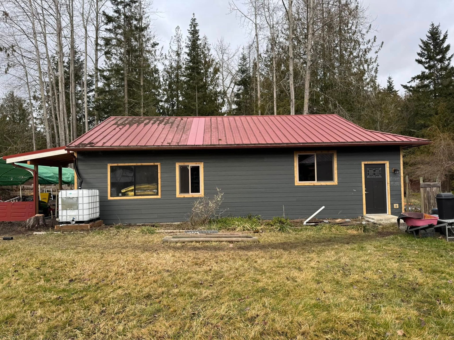 Gray house with red metal roof, surrounded by trees and a grassy yard.