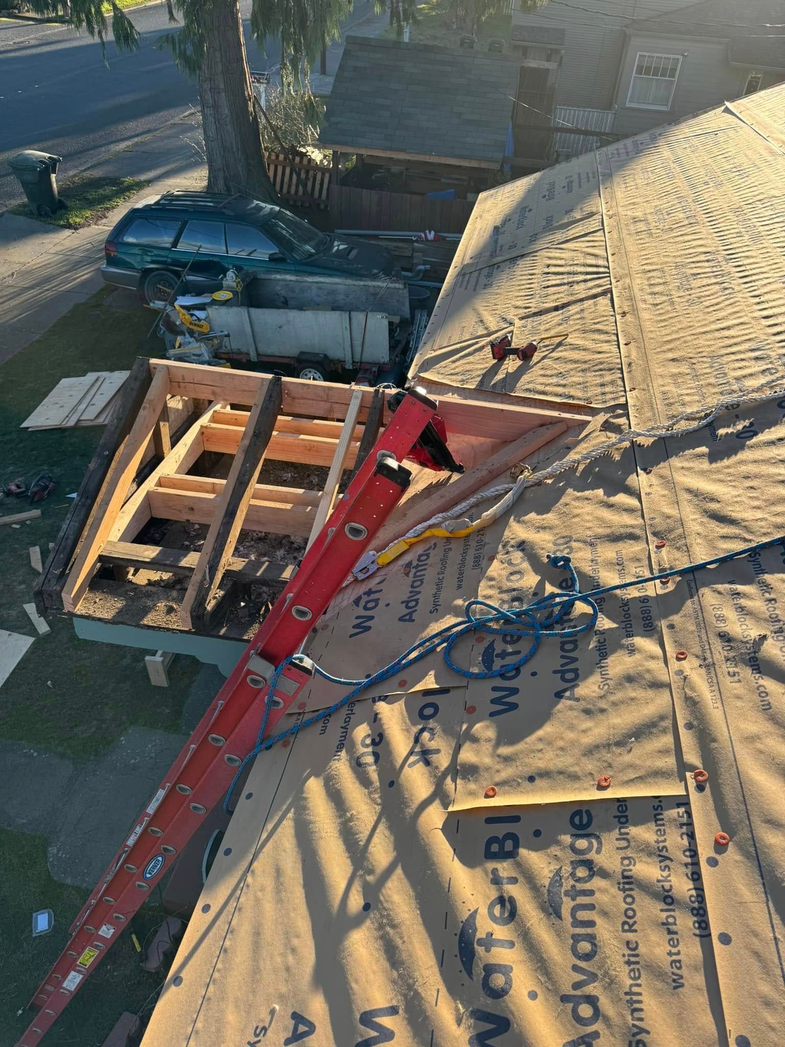 Rooftop construction: Ladder on a roof with new wooden framing, water barrier, and surrounding houses.