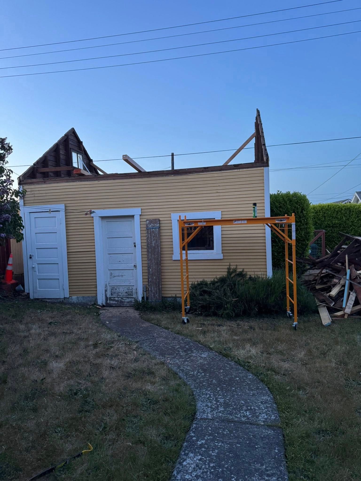 Partially demolished yellow shed with white doors, surrounded by debris, under a blue sky.