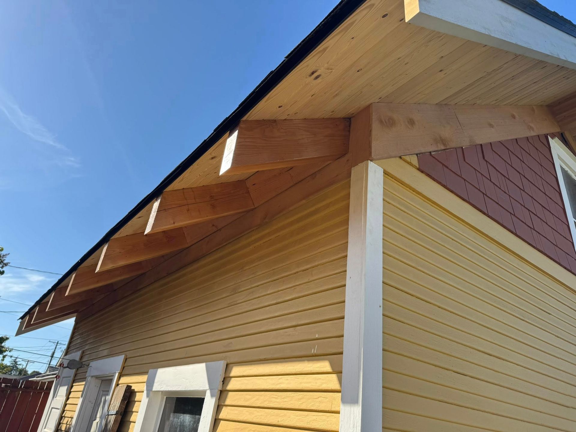 Yellow house with wooden roof supports, partially constructed. Blue sky background.