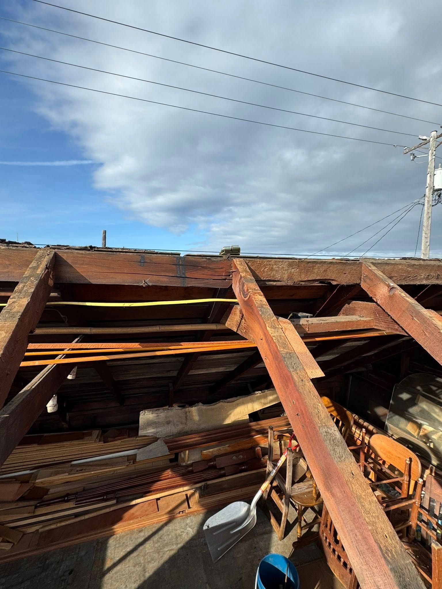Decayed roof structure, wooden beams exposed. Sky above with power lines and utility pole.