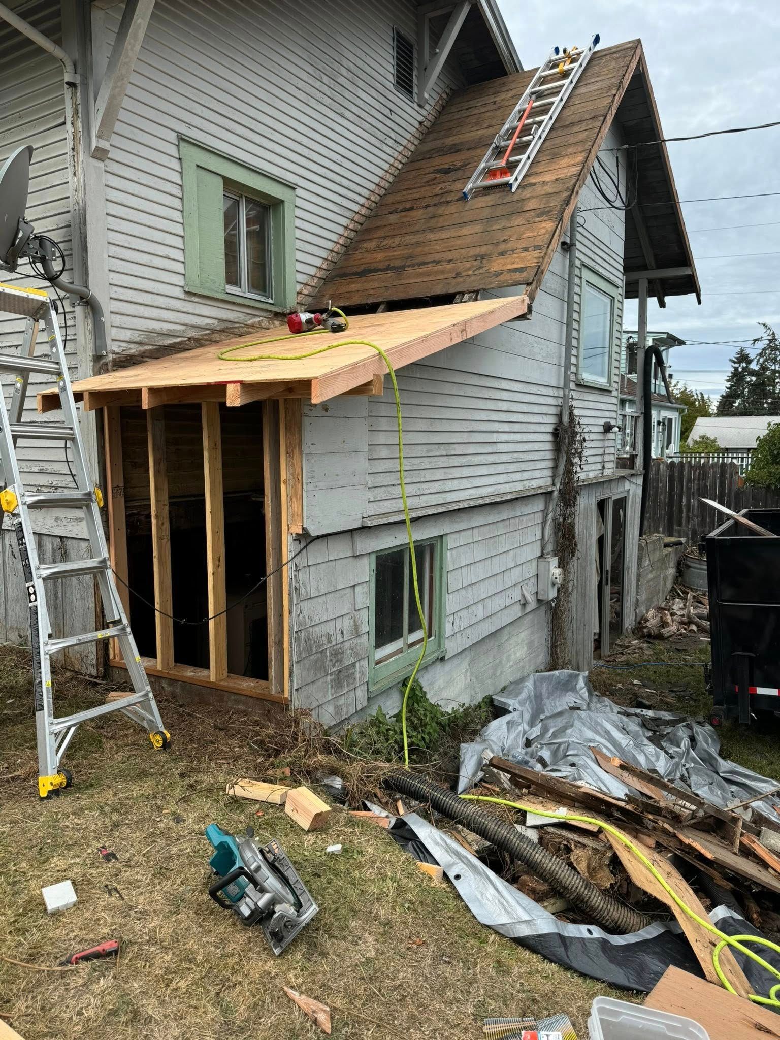 House under construction; extension framing with lumber, ladder, and debris in the yard.