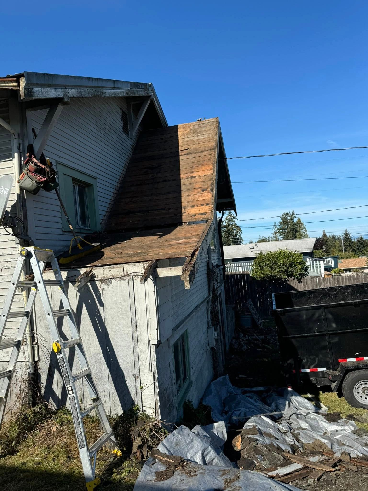 House exterior with brick chimney being worked on; ladder, construction materials, and a dumpster visible.
