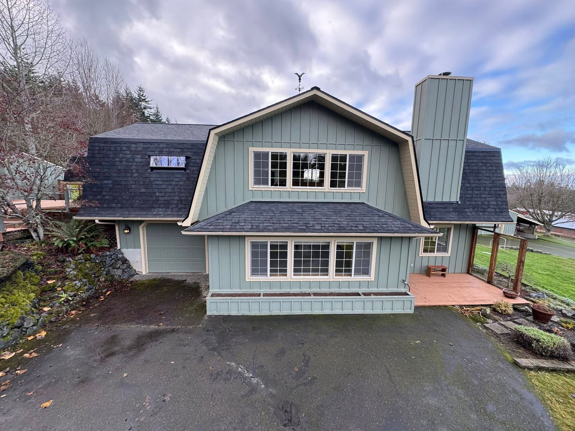 A two-story blue-green house with a dark roof and chimney, set against a cloudy sky.