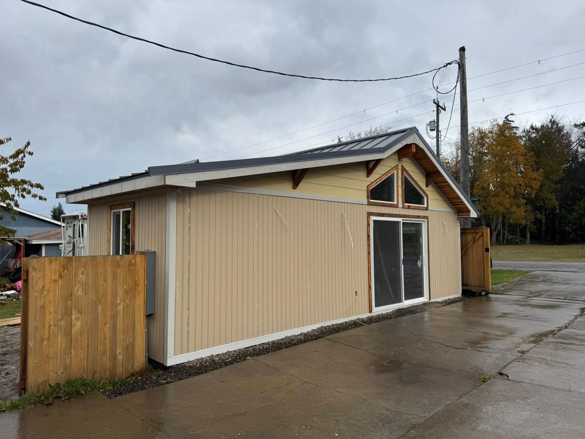 Tan building with a dark roof and large sliding glass door. Wooden fence in front on a cloudy day.