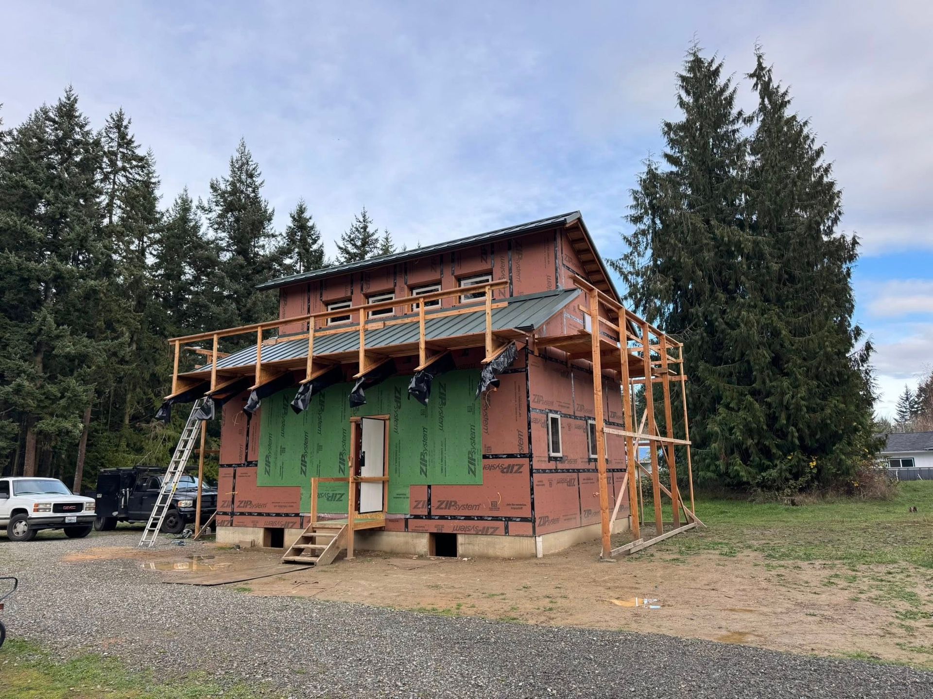 House under construction with scaffolding; green wrap, brown siding, and light brown wood beams.