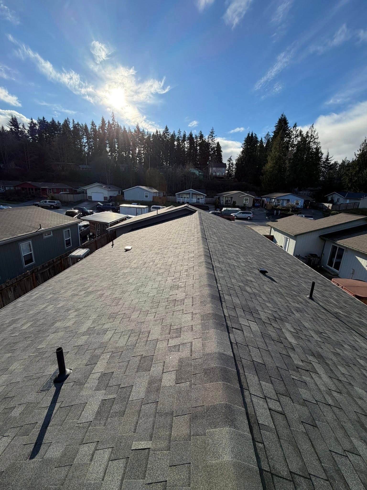 Rooftop view of asphalt shingles, overlooking parked RVs and trees under a bright sky.