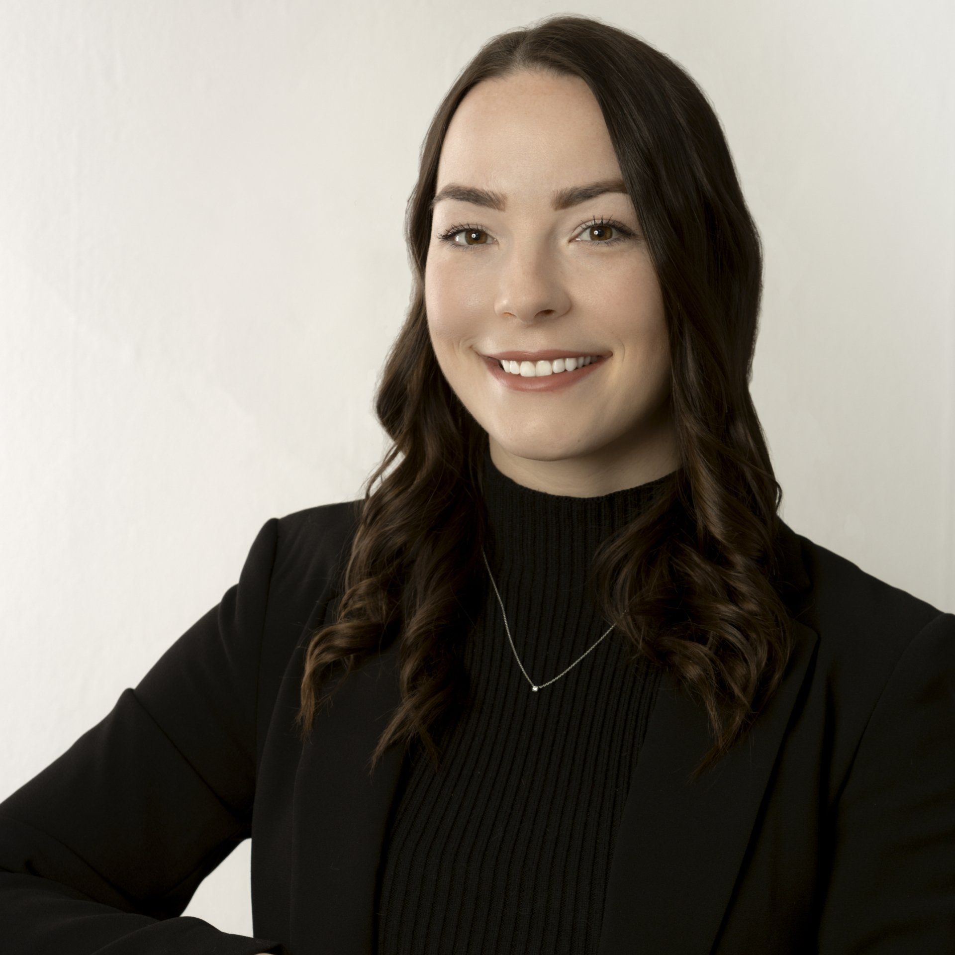 Smiling woman with dark hair wearing a black top and blazer against a light background