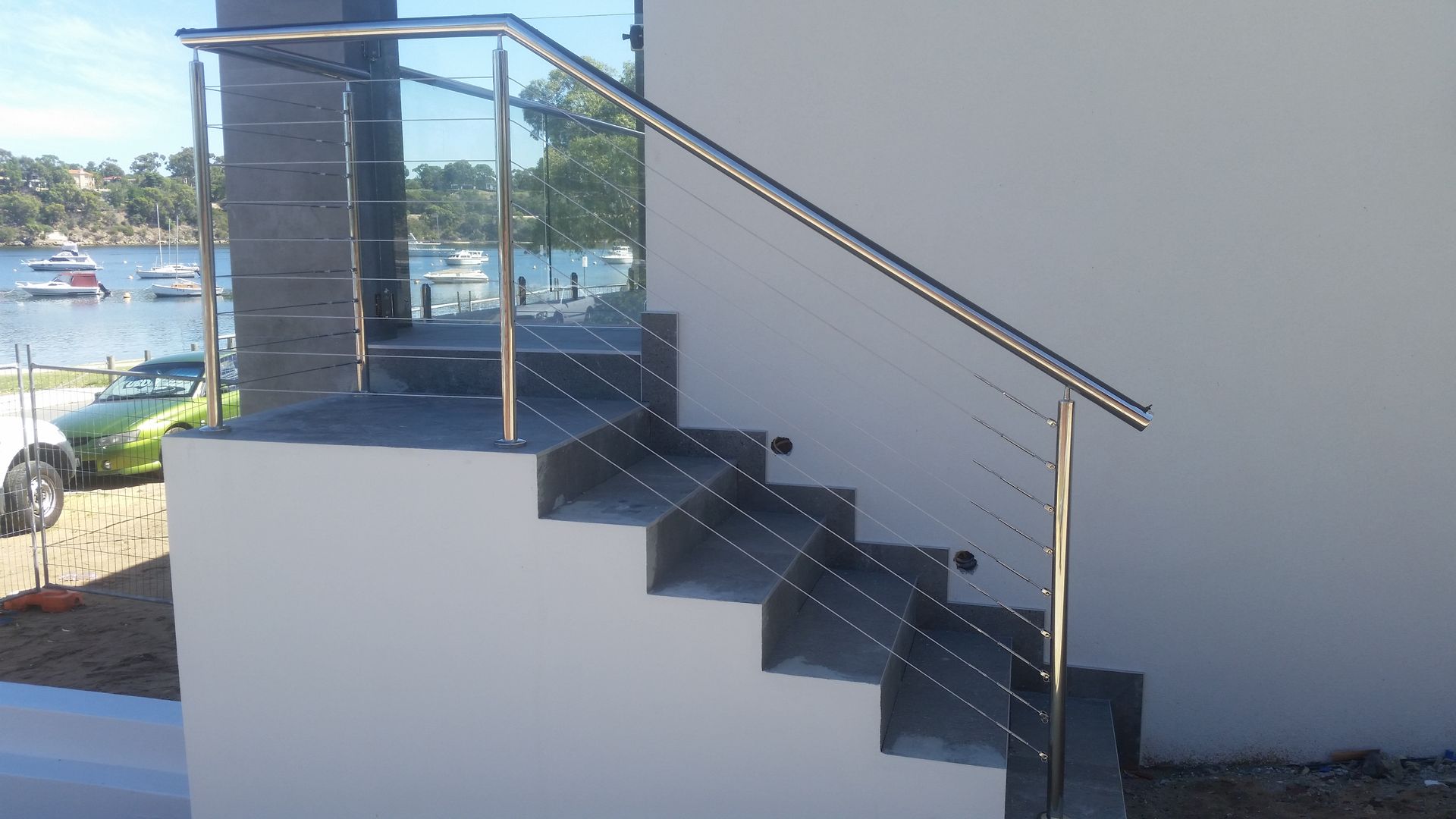 Exterior staircase with stainless steel handrails, overlooking a body of water with boats.
