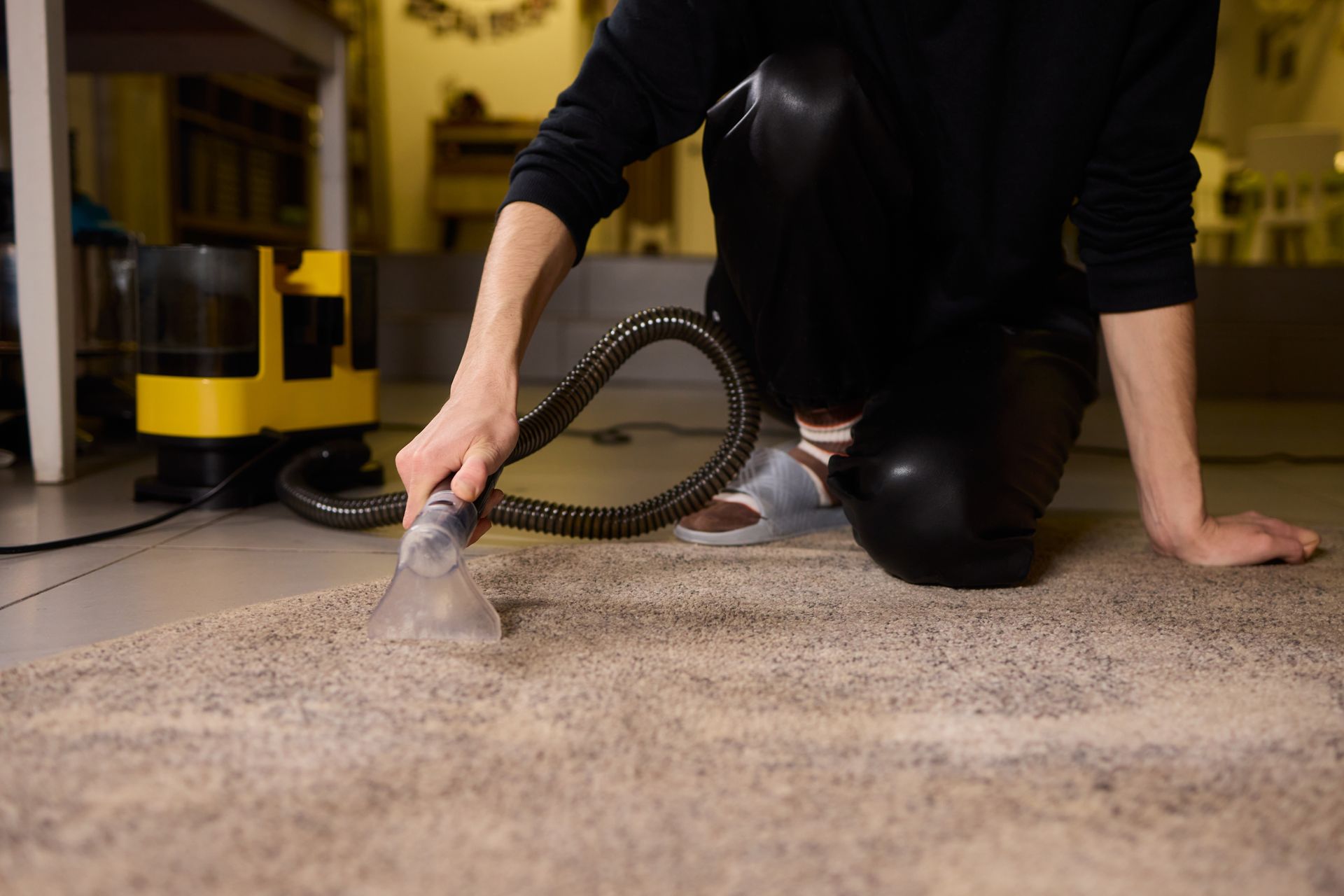 Person vacuuming a beige carpet with a hose attachment in a home interior