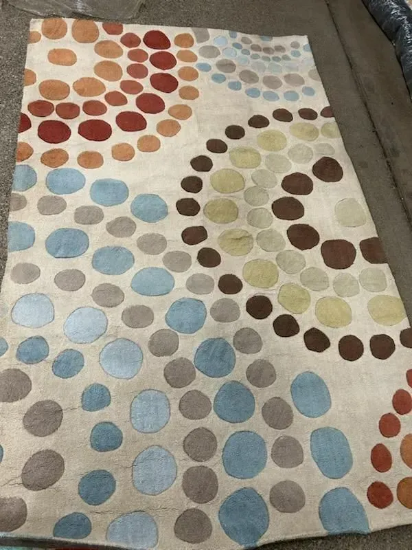 Cream rug with blue, brown, orange, and green polka-dot swirl pattern on a carpeted floor