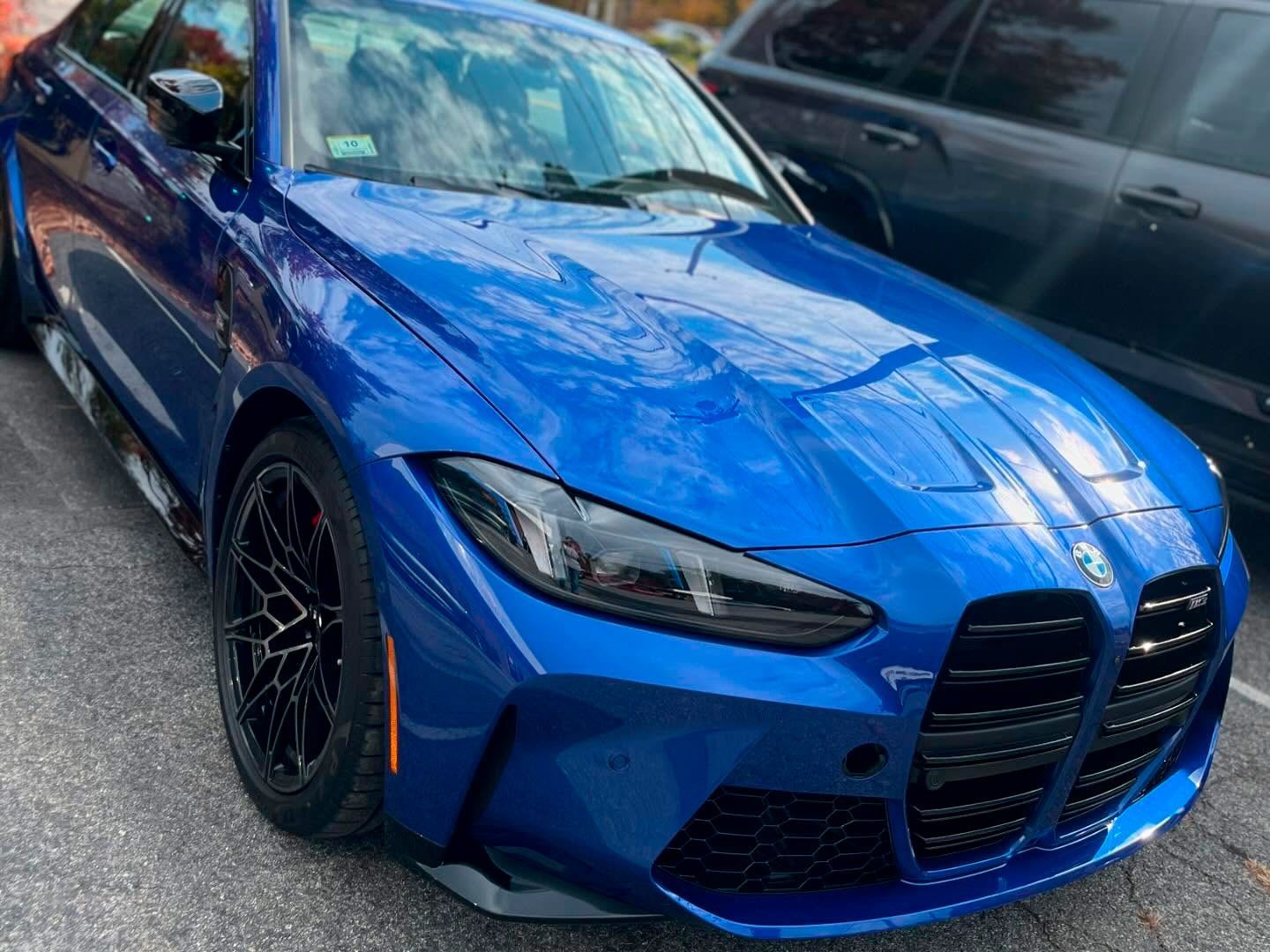 A blue bmw m3 is parked next to a black suv.