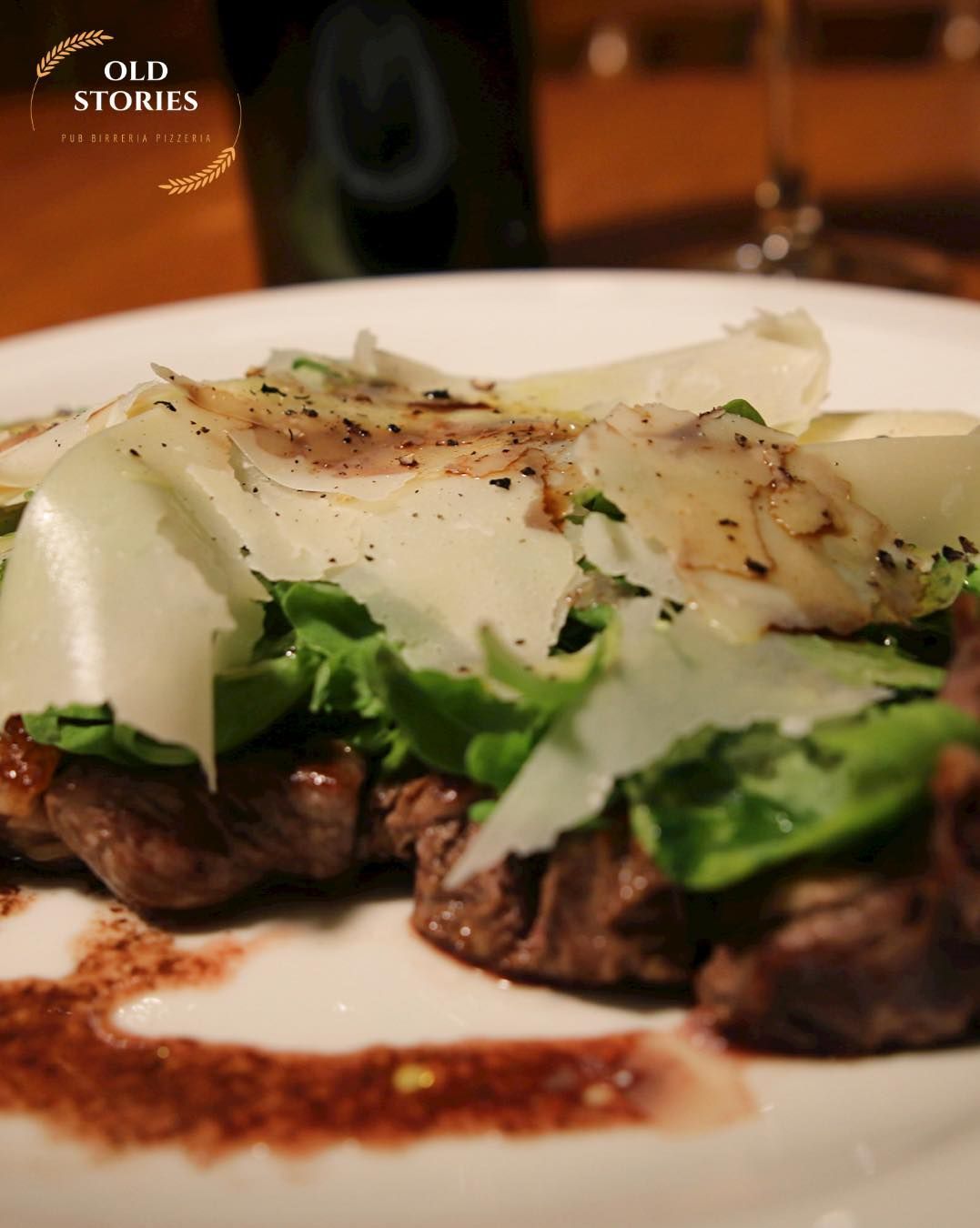 Medaglioni di manzo con rucola, parmigiano grattugiato e un filo di aceto balsamico su un piatto bianco.
