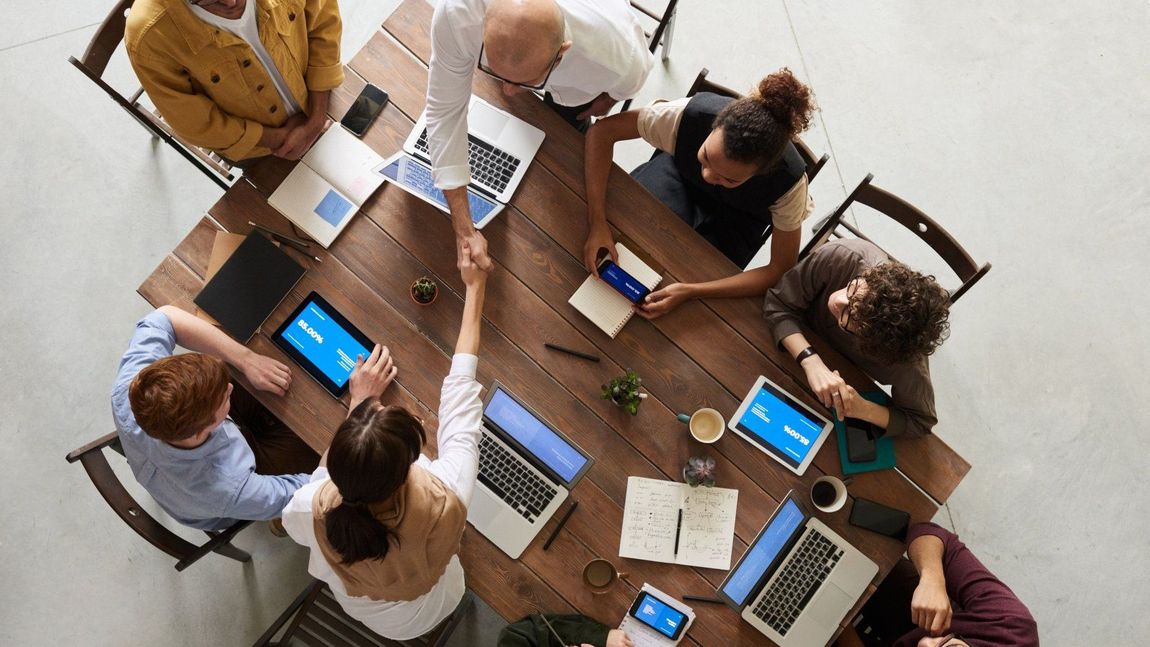 A group of people are sitting around a table shaking hands.