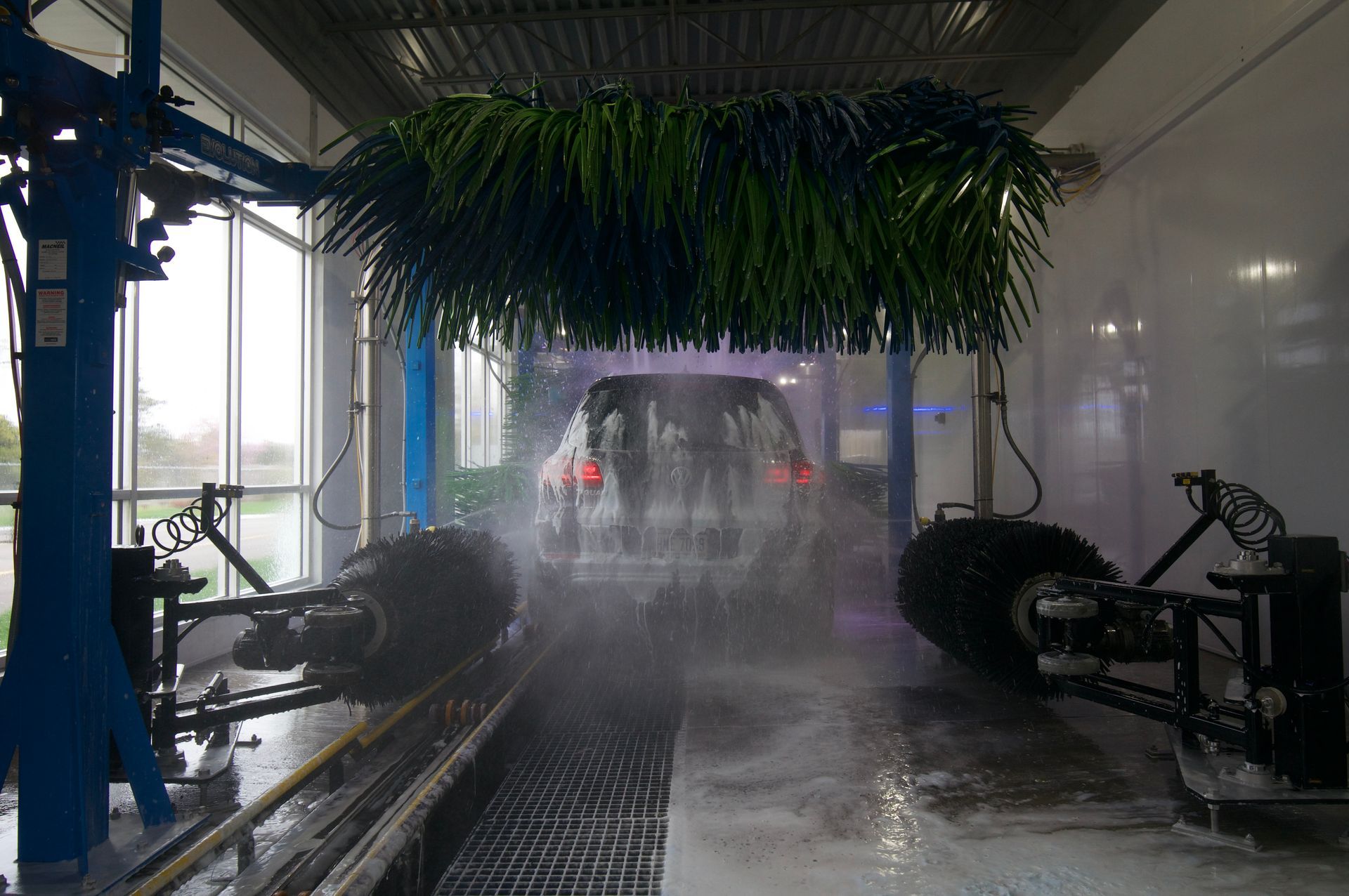 Car wash tunnel spraying water on a vehicle as rotating brushes scrub it under bright lights