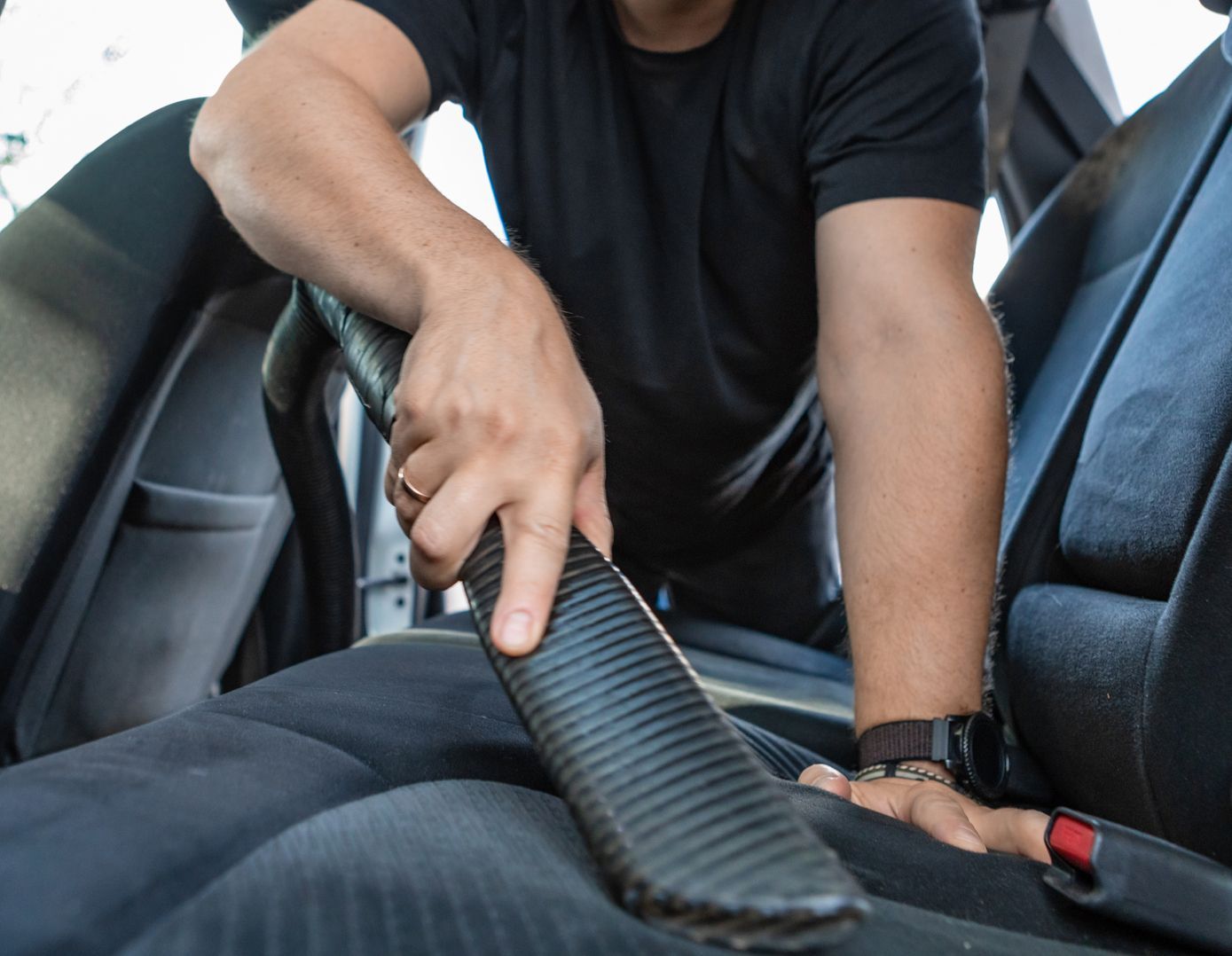 Person vacuuming a car seat with a handheld nozzle inside a vehicle interior