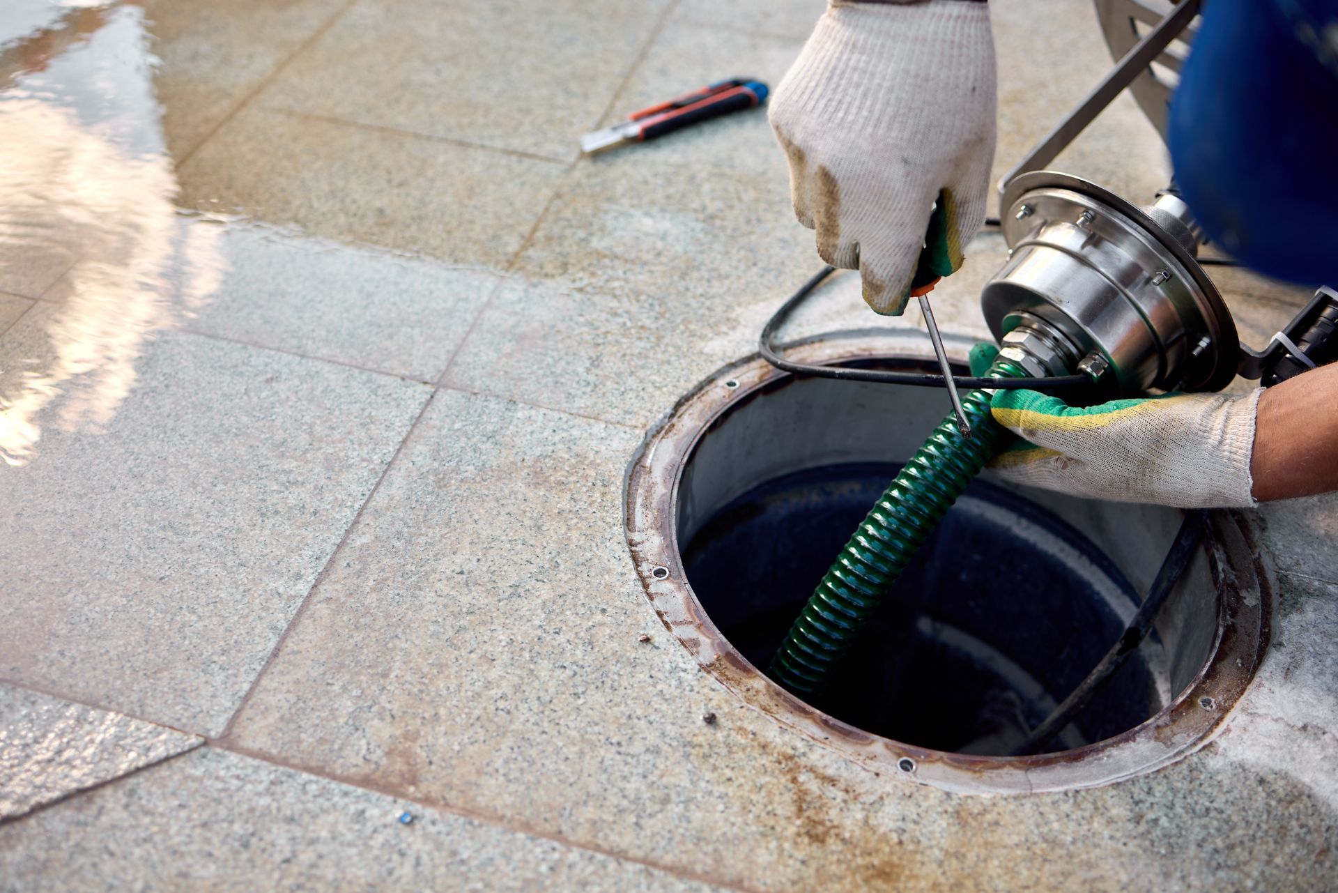 A man cleans a drain using a hose, directing water into the opening to remove debris and dirt.
