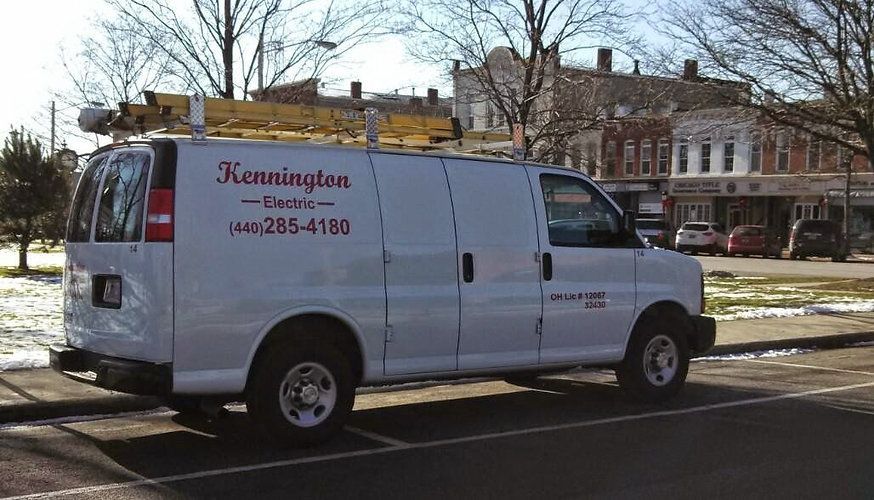 A white van with a ladder on top of it is parked in a parking lot.