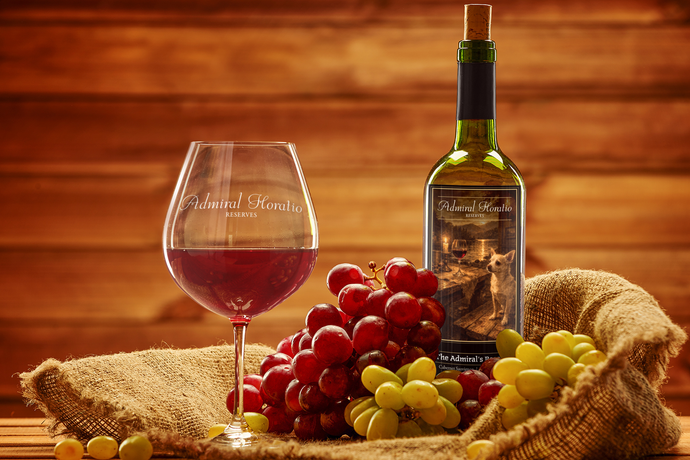 Wine bottle, glass of red wine, and grapes on a rustic burlap cloth against a wooden background.