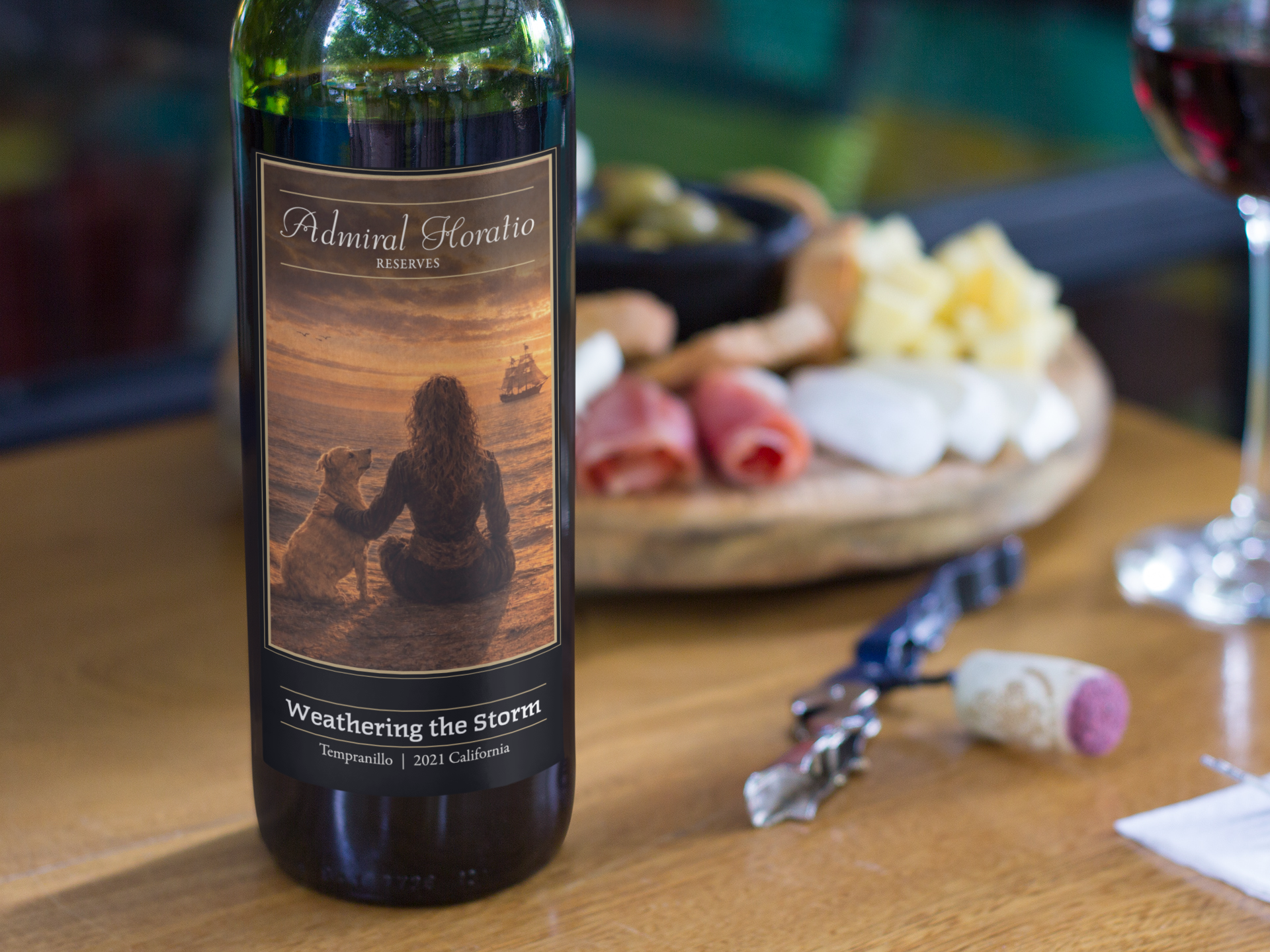 Wine bottle on a wooden table with cheese, sliced meats, and a glass of red wine in the background