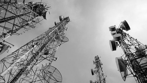 A black and white photo of a bunch of antennas against a cloudy sky.