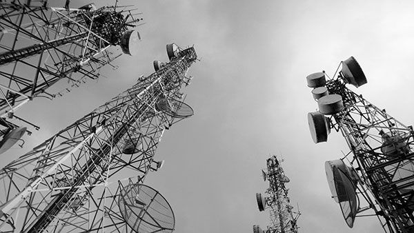 A black and white photo of a group of telephone towers against a cloudy sky.