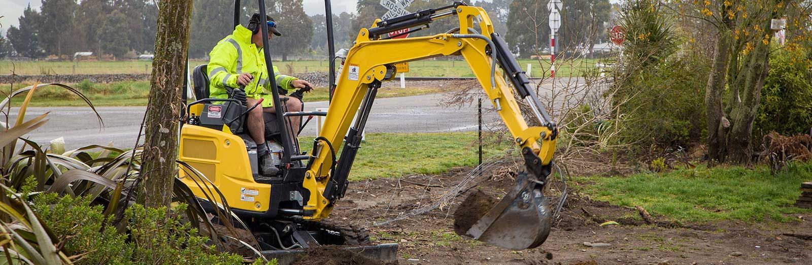 A man is driving a small yellow excavator in a field.