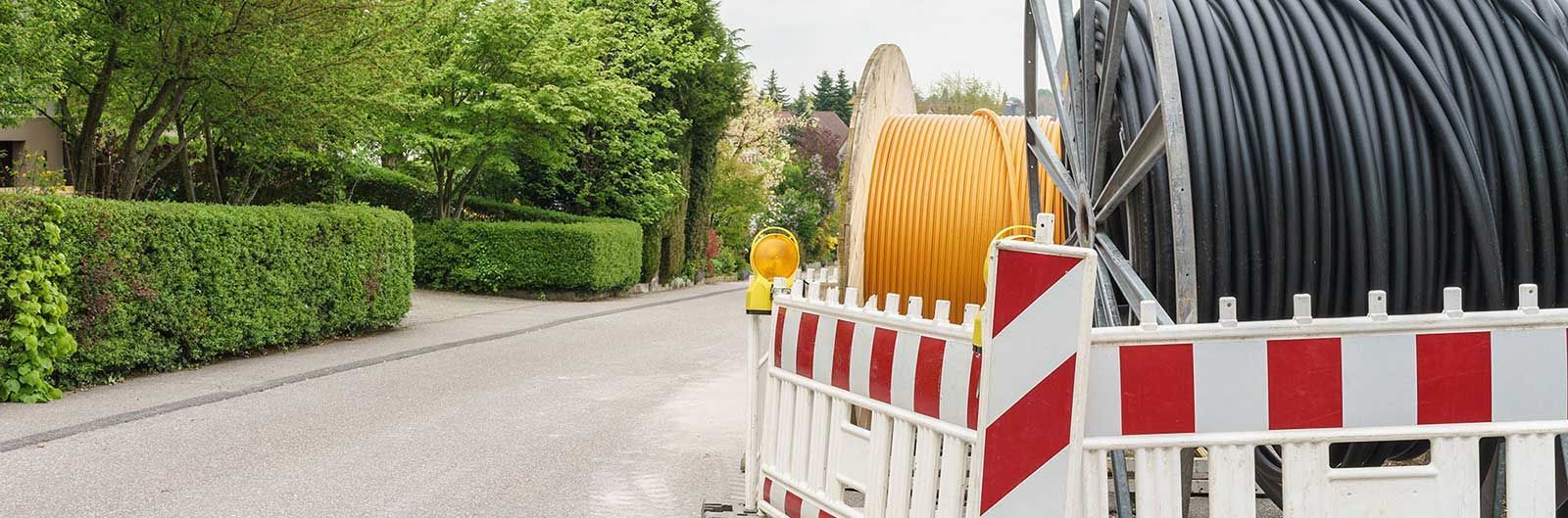A large spool of cable is sitting on the side of a road next to a fence.