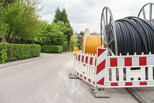 A large spool of electrical wires is sitting on the side of a road next to a fence.