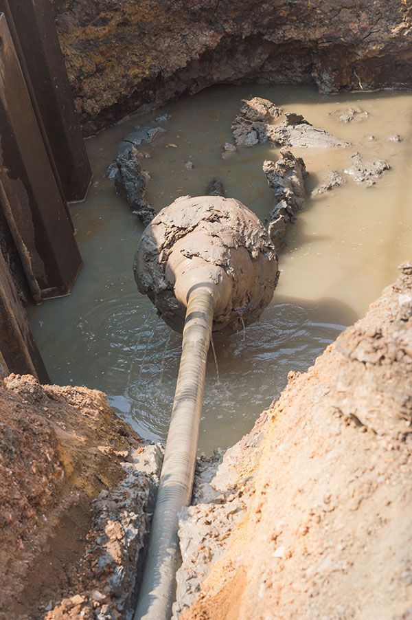 A muddy pipe is coming out of a hole in the ground.