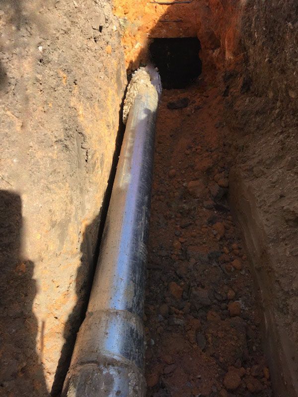 A pipe is laying in the dirt next to a hole in the ground.