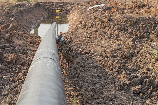 A large pipe is going through a hole in the ground.