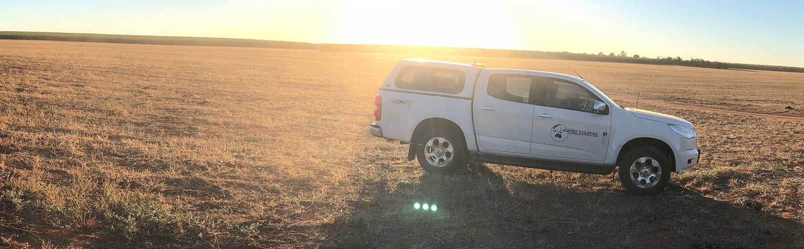 A white truck is parked in a field at sunset.